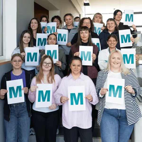 Weibliche Kollegen von NETZSCH-Feinmahltechnik halten stolz ein "M" hoch, symbolisierend Zusammenhalt und Vielfalt am Internationalen Frauentag.