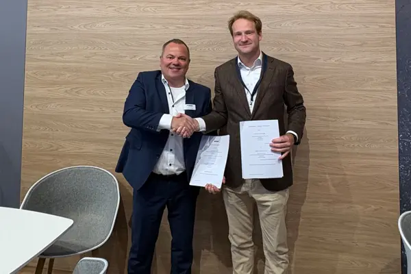Matthias Kapp of NETZSCH and Julian Lekner of DST shake hands holding partnership documents, celebrating Sheartex technology collaboration.