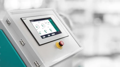 Painel de controle de uma máquina NETZSCH com uma interface digital touchscreen com medidores e um botão de parada de emergência.