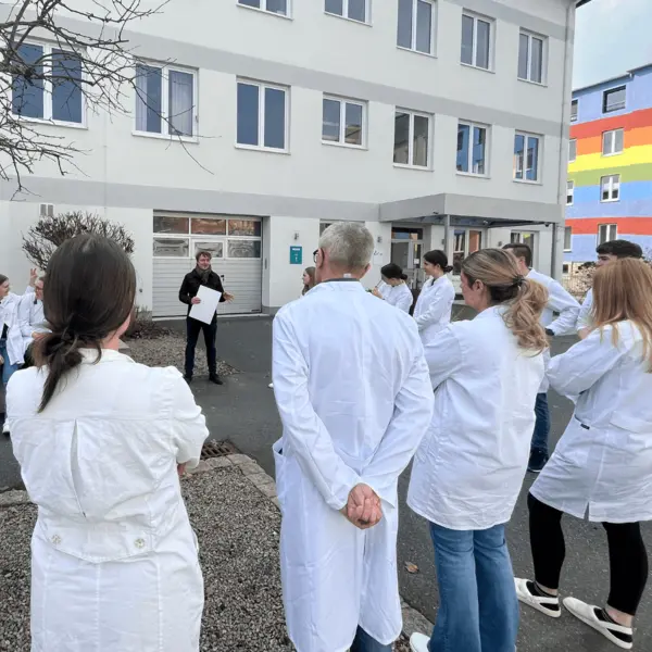 Studenten in weißen Kitteln hören einem Vortrag im Freien zu, während sie sich in der Nähe des NETZSCH Standorts versammeln.