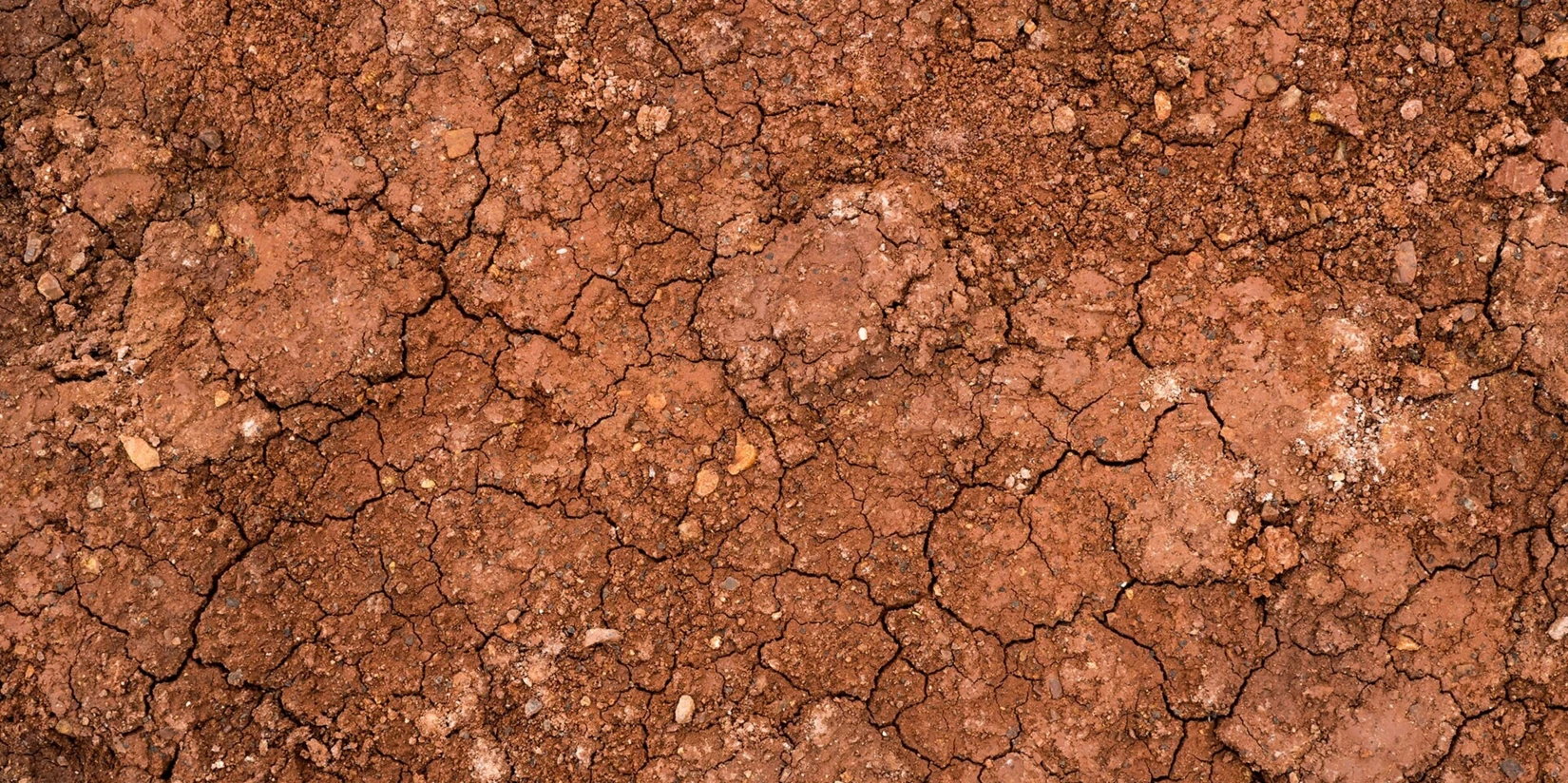 Textura de solo marrom-avermelhado rachado, mostrando formações naturais de terra ideais para ilustrar processos de moagem e dispersão.