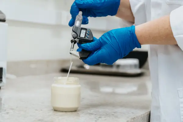 Eine Person mit blauen Handschuhen misst die Viskosität einer cremigen Substanz in einem Labor, um die Qualität zu überprüfen.