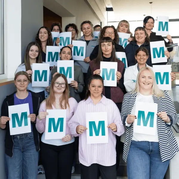 Des collègues féminines de NETZSCH tiennent des pancartes avec un "M" dans le cadre d'une initiative photo mondiale à l'occasion de la Journée internationale de la femme, célébrant la diversité et la force.