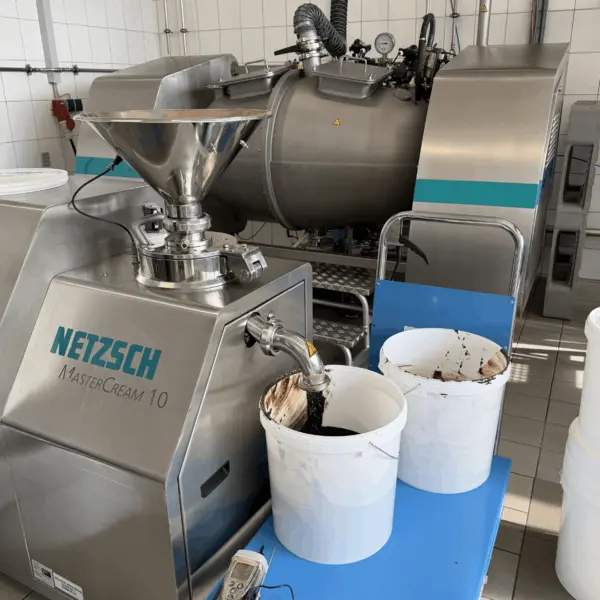 Der NETZSCH MasterCream 10 verarbeitet Kakaomasse in der Lebensmitteltechnologie, mit zwei Behältern für fertige Produkte.