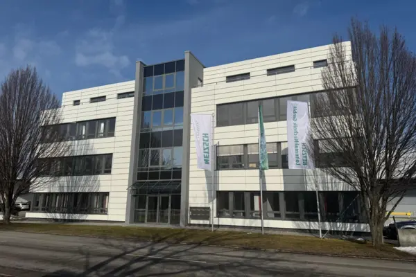 Modernes Unternehmensgebäude der NETZSCH Lohnmahltechnik GmbH in Bobingen mit Fahnen im Vordergrund und klarem blauen Himmel.
