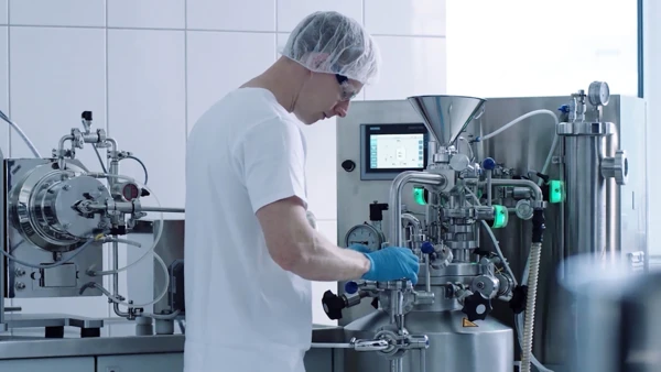 Ein Techniker mit Handschuhen arbeitet an einer modernen Mahlmaschine in einem Labor, fokussiert auf die Prozessoptimierung.