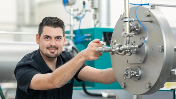 Ein Techniker arbeitet an einer Maschine zur Mahl- und Dispergiereinheit von NETZSCH, verkörpert Fachkompetenz und technische Präzision.